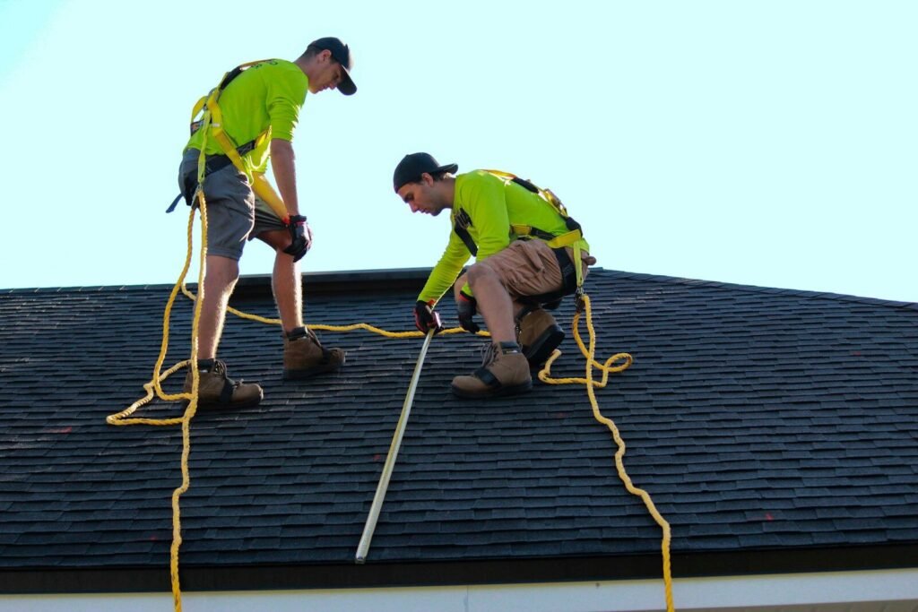Two workers on a dark shingled roof.