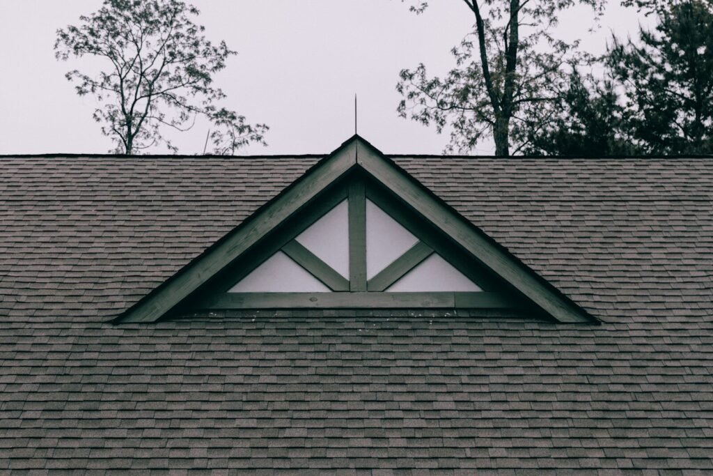 A shingled house roof with a triangular gable window