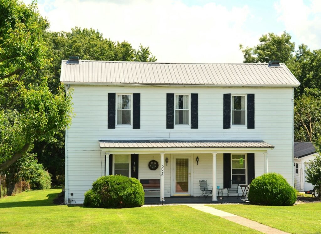 A two-story white house with black shutters and a front porch on a lawn